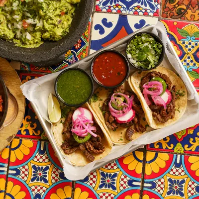 Ett bord med tacos, guacamole och salsor på mönstrat kakel