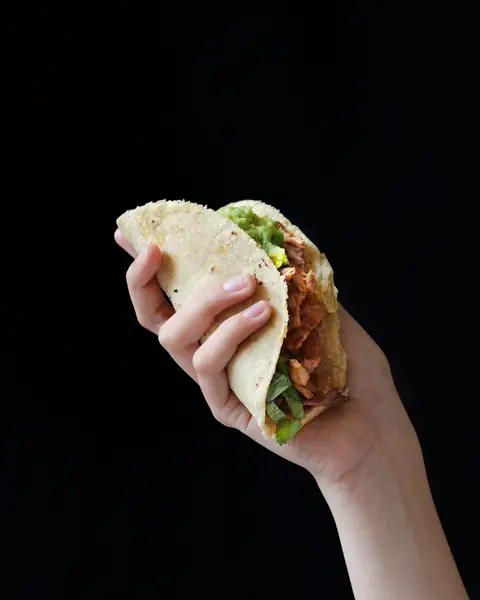 En hand håller en taco mot svart bakgrund