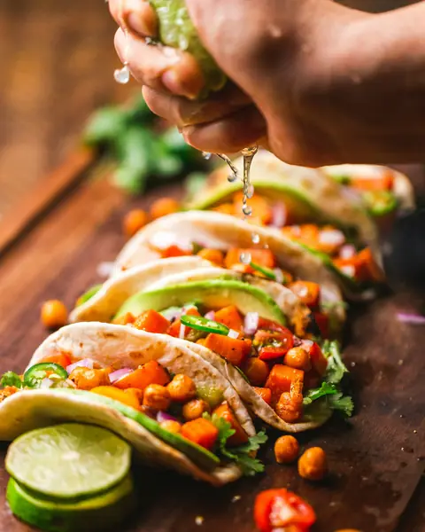 En hand pressar lime över tacos med kyckling och tomat