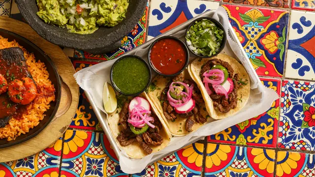 Ett bord med tacos, guacamole och salsor på mönstrat kakel